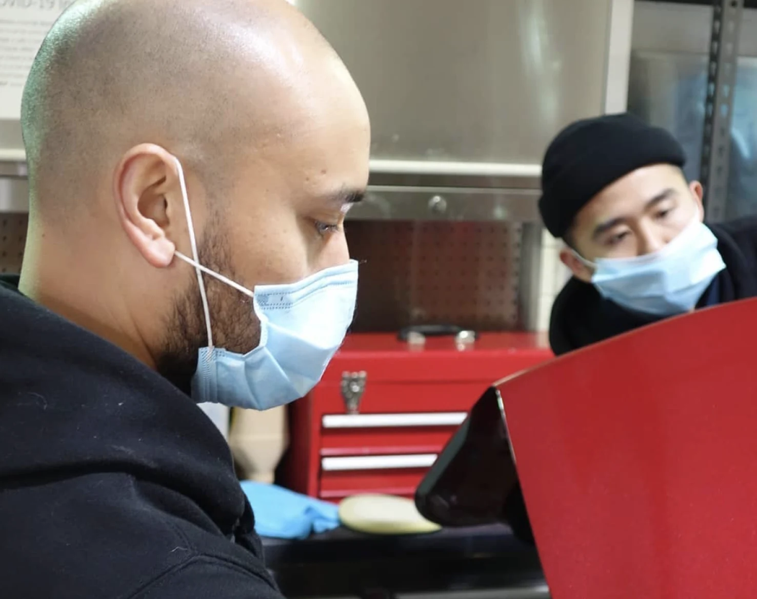 Two technicians in masks working on a red car