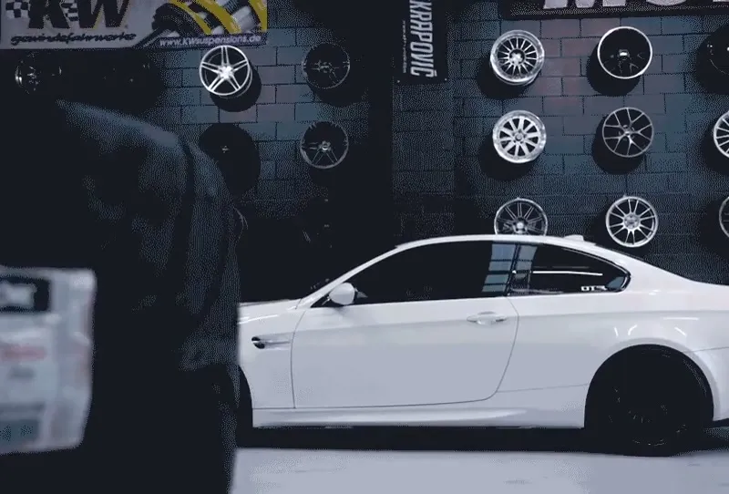 White BMW coupé in front of a wall of wheels