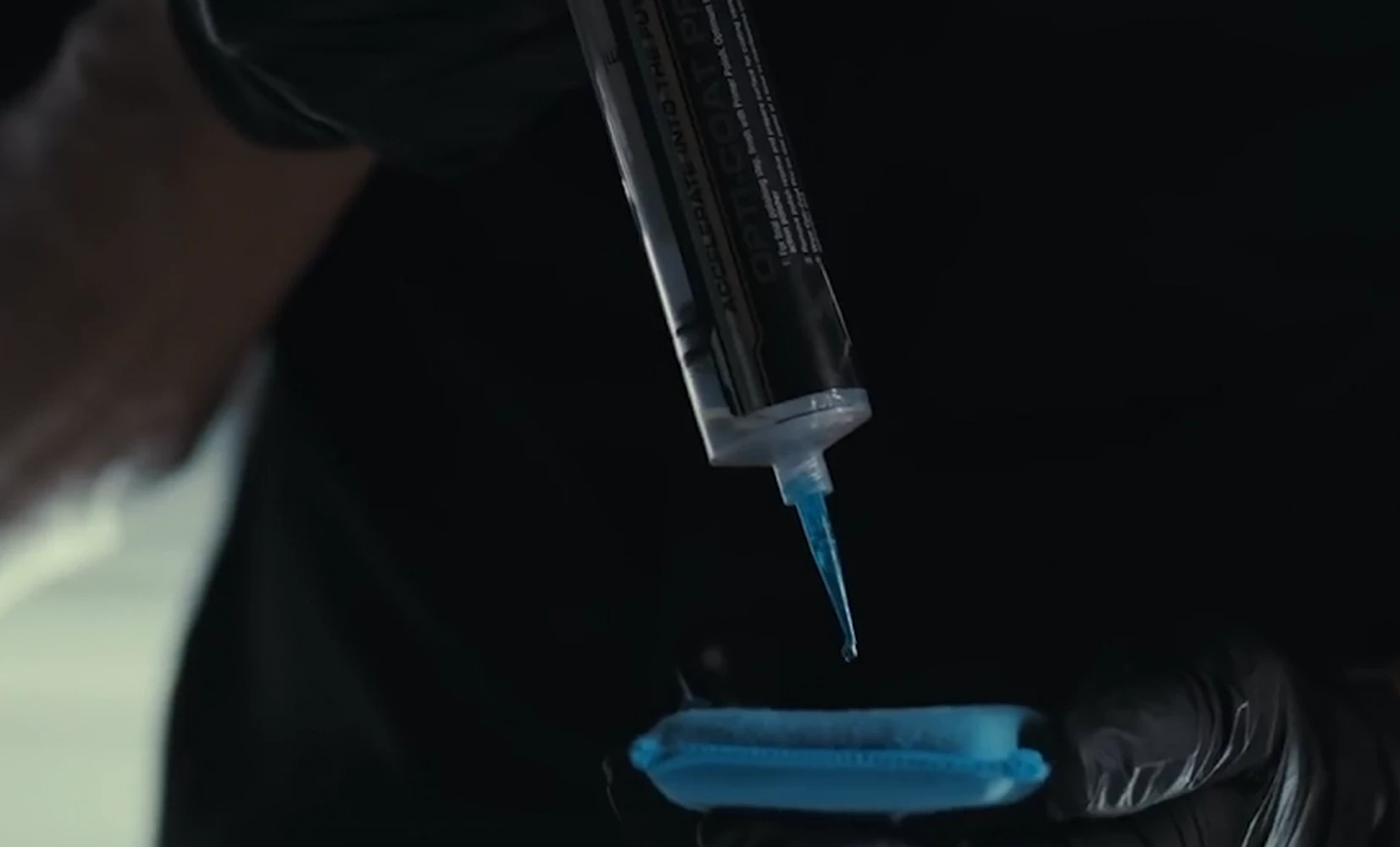 Syringe dispensing product onto a blue applicator pad