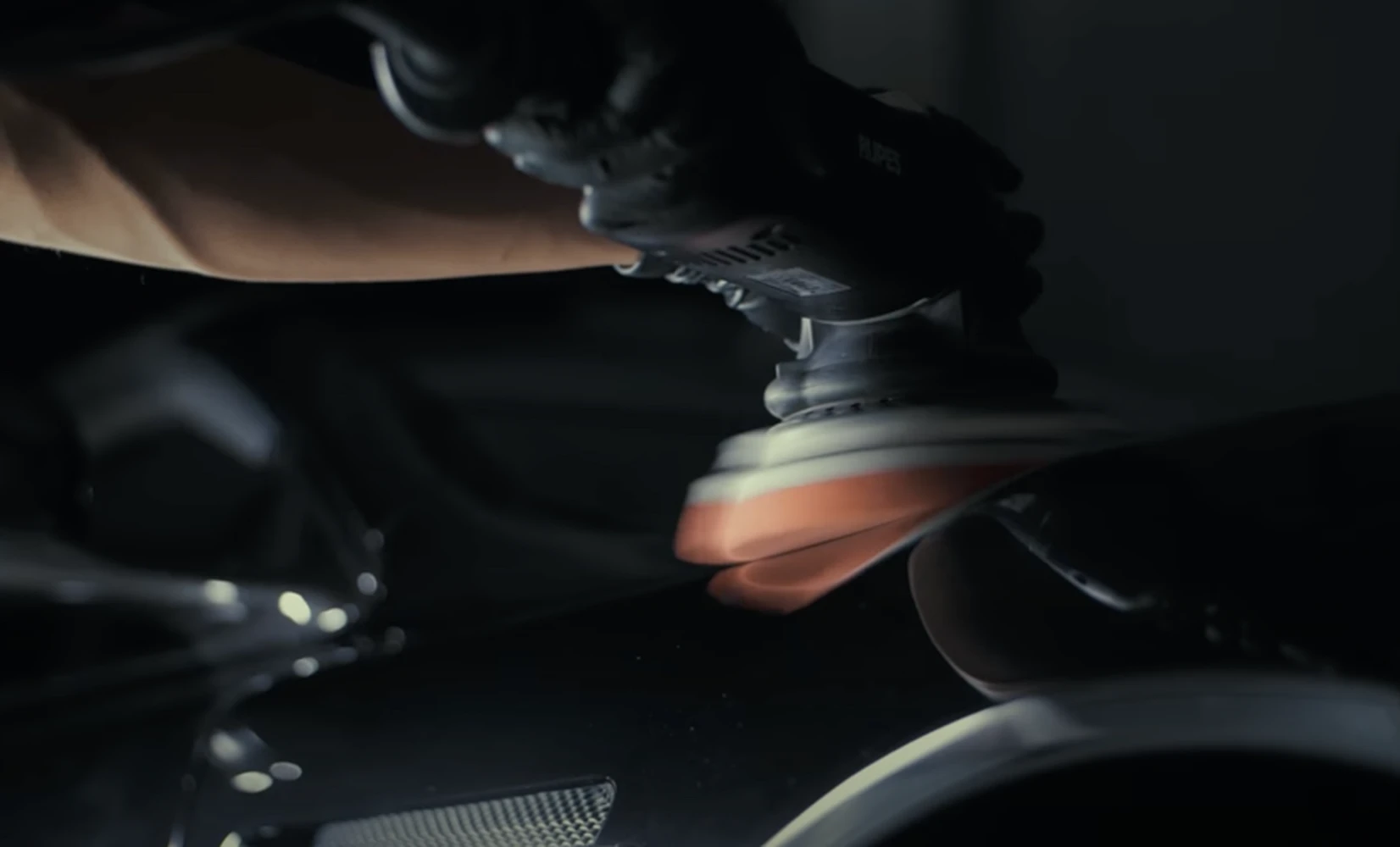 Gloved hands machine-polishing a car door